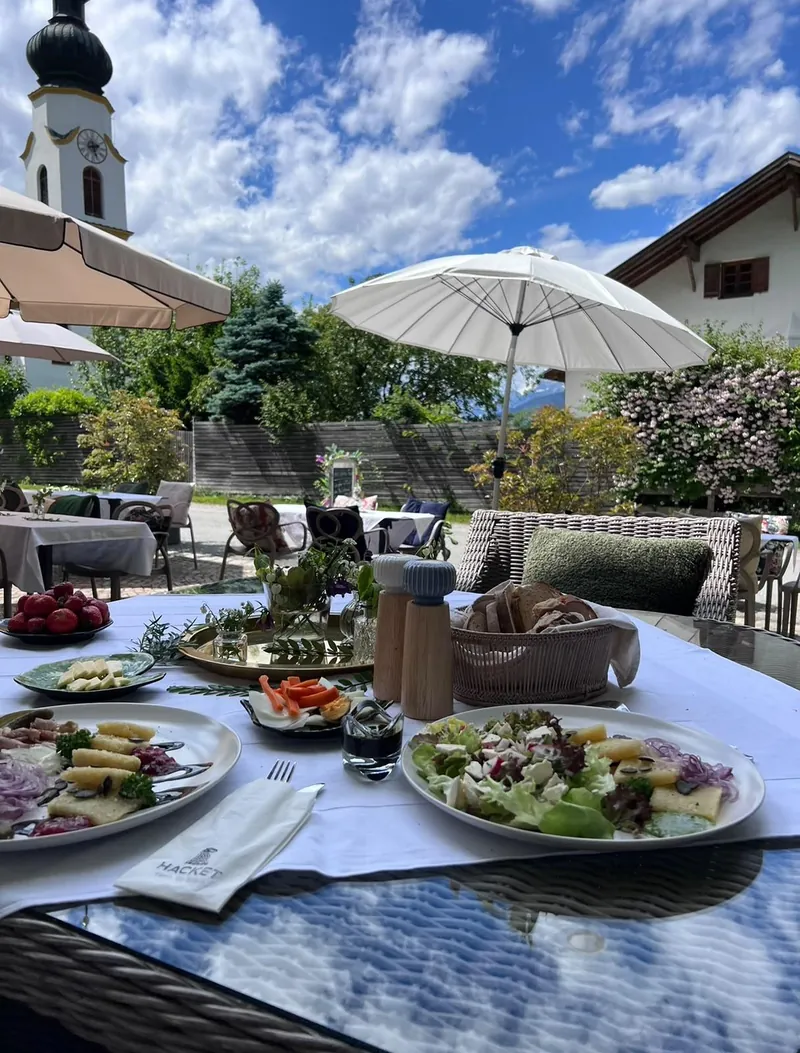 Gedeckter Gartentisch mit Sonnenschirmen und der Aflinger Kirche im Hintergrund, ohne Personen